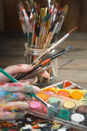 Female hands with paint brushes and palette on wooden table, closeupの写真素材