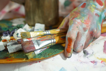 Close-up of female hands with paint and brushes on the tableの写真素材