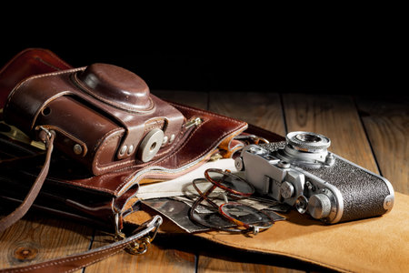 Old camera in a brown leather case on a wooden table. Black background.