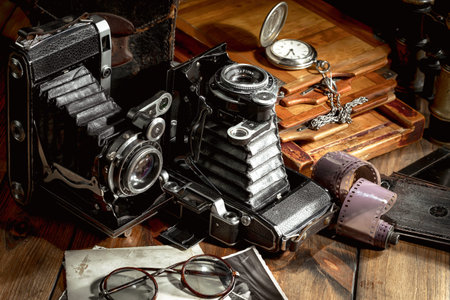 Old camera on an old wooden table with a watch and glasses.