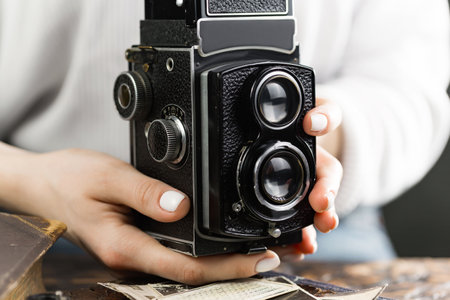 Female hands holding a vintage camera on a wooden table, close-upの写真素材