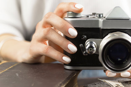 Female hand with white manicure on nails holds a retro camera.の写真素材