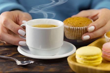 Female hands holding a cup of coffee and macaroons on a wooden tableの写真素材