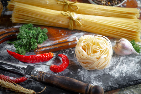 Raw pasta with ingredients for cooking on the table in composition with kitchen accessoriesの写真素材