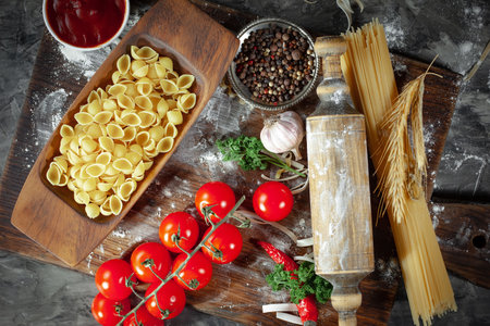 Different types of pasta on a wooden table with tomatoes, garlic and spicesの写真素材