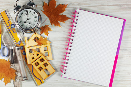 School supplies, alarm clock, notebook and autumn leaves on white wooden background. Top view with copy spaceの写真素材