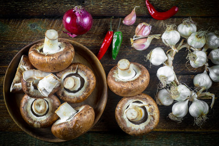 Fresh champignon mushrooms, garlic and chili pepper on wooden backgroundの写真素材
