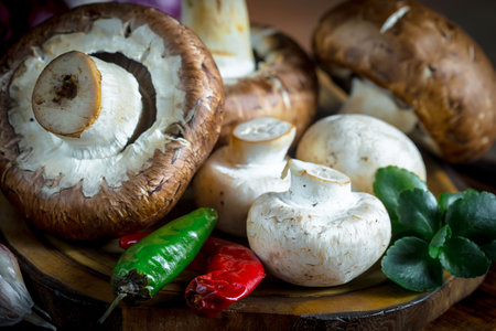 Champignon mushrooms with chili pepper and green leaf on wooden plateの写真素材