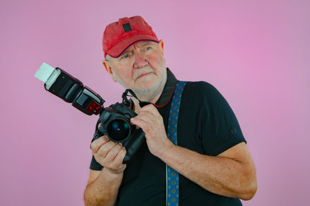 Portrait of a senior photographer with a camera on a pink background