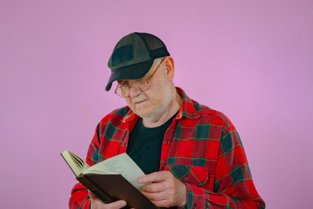 Portrait of an elderly man reading a book on a pink backgroundの写真素材