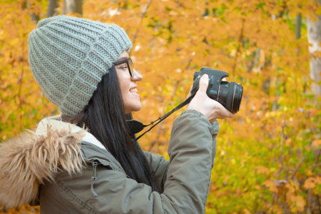 Beautiful young woman taking a photo with a camera in the autumn forest