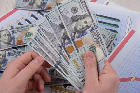 Hands counting dollar banknotes on a table with graphs and charts