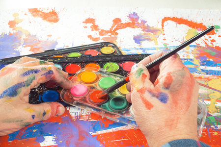 Hands of the artist with a brush and paints on a palette