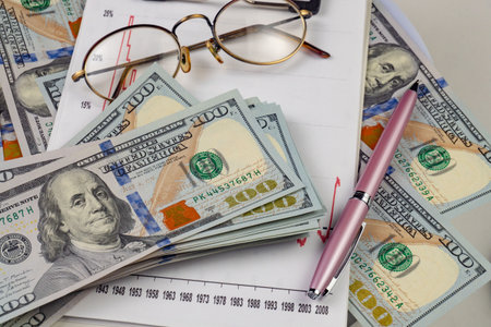 Close-up of one hundred dollar bills, glasses and pen on white background