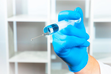 Hand in blue glove holding a syringe with a vaccine against virusの写真素材