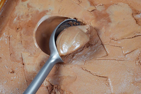 Scoop of chocolate ice cream with spoon on brown background.の写真素材