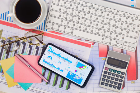 Workplace with smart phone and financial charts on the table. Business