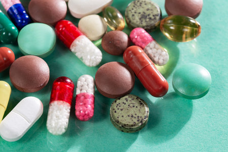 Colorful pills and capsules on green background. Focus on foreground.