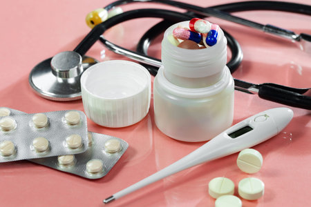 Stethoscope, pills and thermometer on a pink background.
