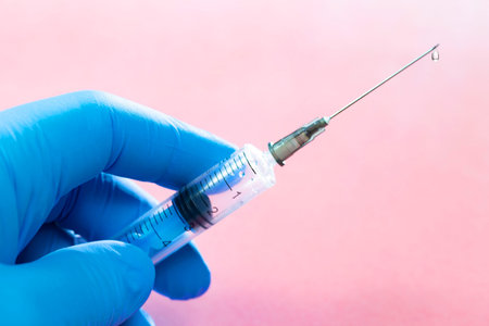 Syringe in the hand of a doctor in blue gloves on a pink background