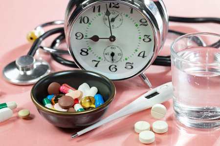 Alarm clock, stethoscope and pills on pink background.