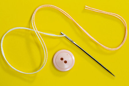 spool of thread, needle and button on a yellow background.