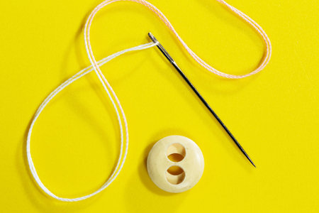 Needle and thread on a yellow background. Sewing accessories.