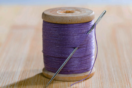 spool of purple thread with needle on wooden background, closeup