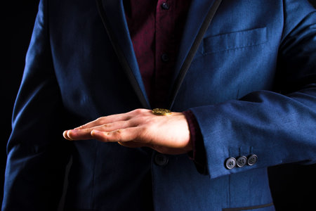 A businessman in a purple suit holds a yellow coin in the palm of his hand.