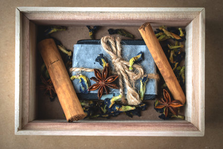 A block of natural carbon soap in a wooden box with cinnamon sticks and dry flowers.の写真素材