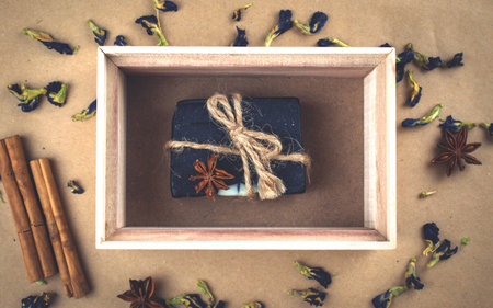 A block of natural carbon soap in a wooden box with cinnamon sticks and dry flowers.の写真素材