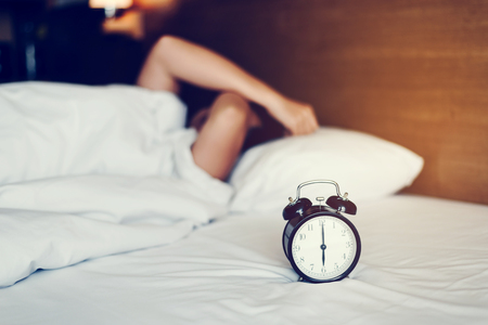 The woman's hand under the blanket reaches out for the alarm clock.の写真素材