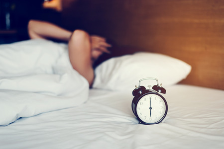 The woman's hand under the blanket reaches out for the alarm clock.の写真素材