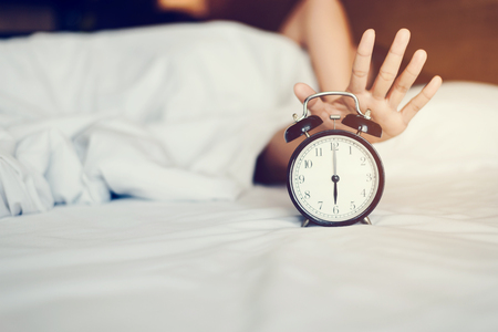 The woman's hand under the blanket reaches out for the alarm clock.の写真素材