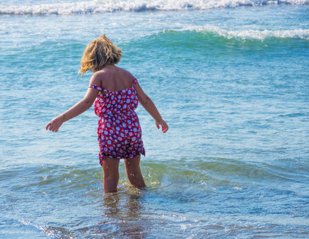 little girl in a red dress goes to sea with wavesの写真素材