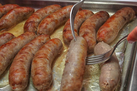 The process of frying home sausages on a tray, turning over withの写真素材