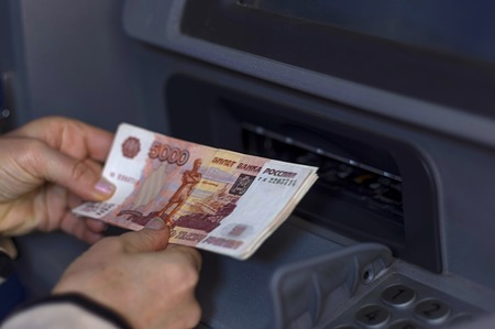 The hand holds a stack of money in front of the open ATM receiveの写真素材