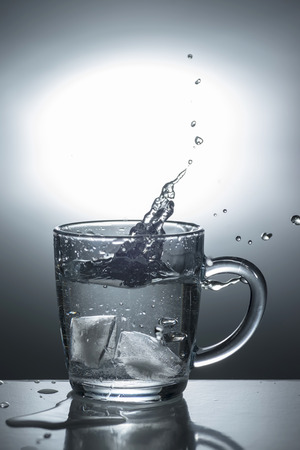 Transparent glass with ice falling into the water, light toningの写真素材