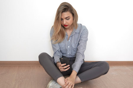 Beautiful young blonde sits on the floor and looks into the phone