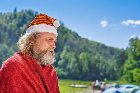 Santa Claus with a beard and a cap on the background of the summer landscape with tourists on a sunny dayの写真素材
