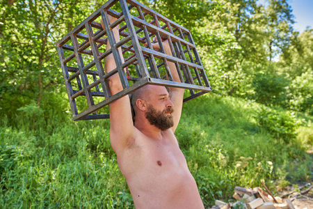 A bearded man with naked torsos holds an iron cage over his head. The concept of liberation, freedom...