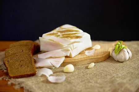 Still life in rustic style, lard with bread and garlic on a burlap, black backgroundの写真素材