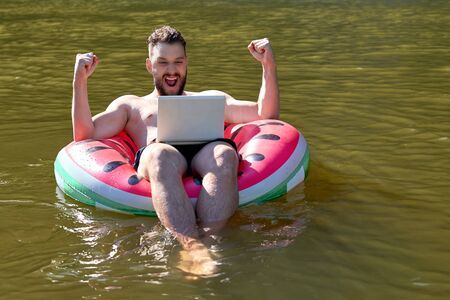 A blogger or freelancer with a laptop floats on a rubber ring. Emotion of delight and joyの写真素材