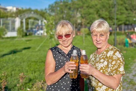 Two elderly ladies holding a transparent plastic beer bottlesの写真素材