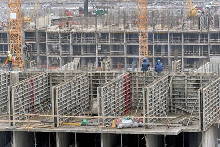 The construction of multi-storey residential complex. two workers sit on their haunches with their backs to the camera on a concrete wallの写真素材