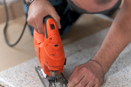 Cut a hole in countertop for a sink, assembling furniture at home. Electric jigsaw in hand,close-up.