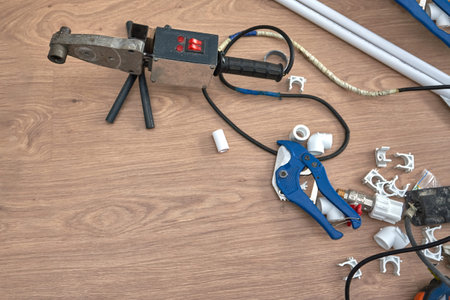 Soldering iron for welding of plastic water pipes on the floor lying next plumbing fittings, top...