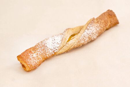 A tube of puff pastry with yellow jam sprinkled with white powdered sugar. Fresh pastries, an assortment of bakery and bakery. Closeup on a light backgroundの写真素材