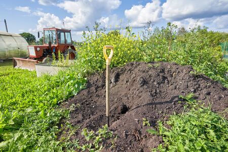 Rural landscape with green grass, a red tractor and a shovel sticking out of the ground. Agriculture in the springの写真素材