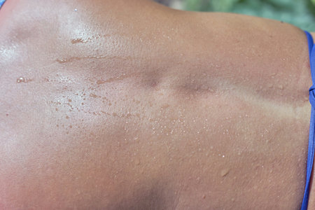 Fragment women's open back with drops of sweat. Sunny summer day, close-up, top viewの写真素材